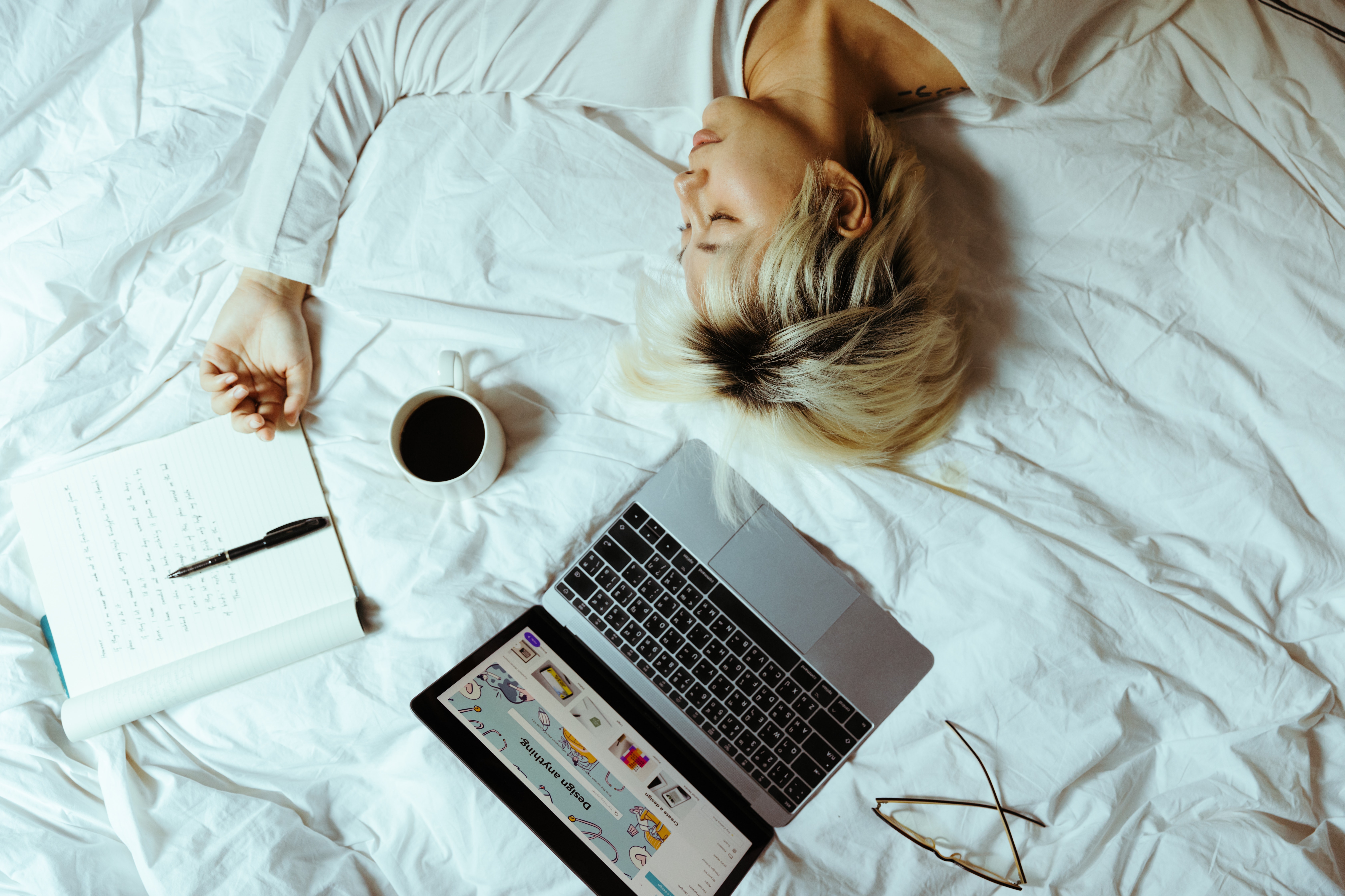 woman sleeping on bed with computer, coffee, and book