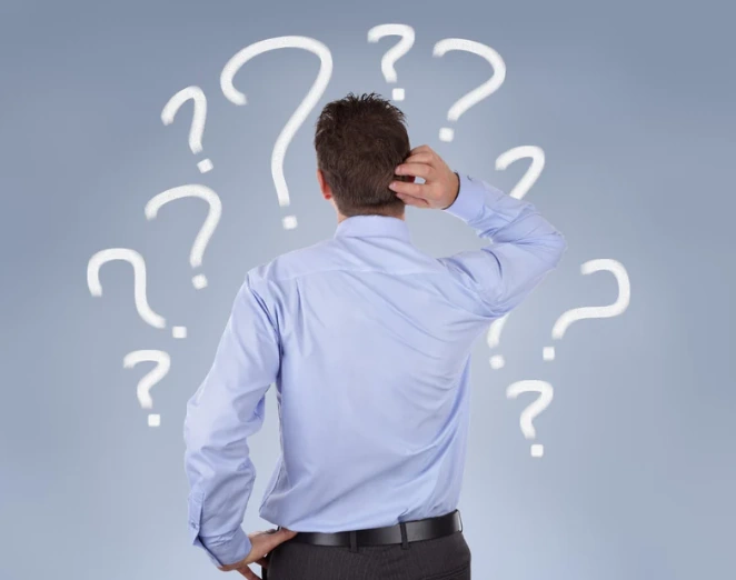 man surrounded by question marks scratching his head